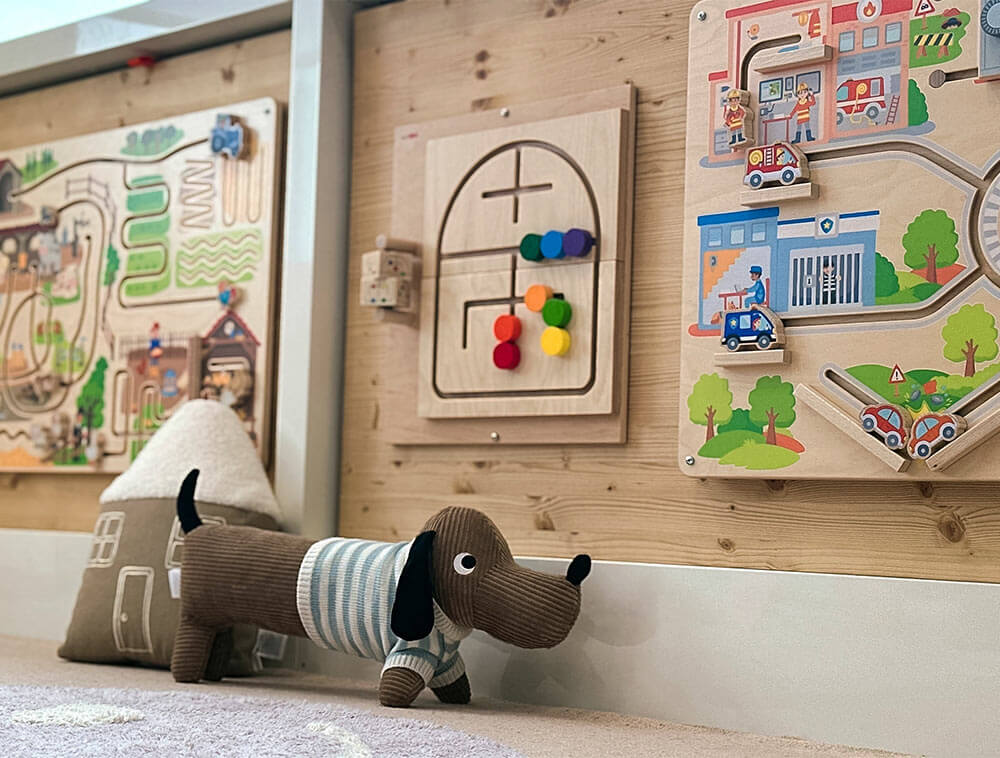 Kinder-Spielbereich im Schreiber Kids Adventureland
Wilnsdorf mit an der Wand montierten Motoriktafeln für Kleinkinder
und gemütlicher Spielecke