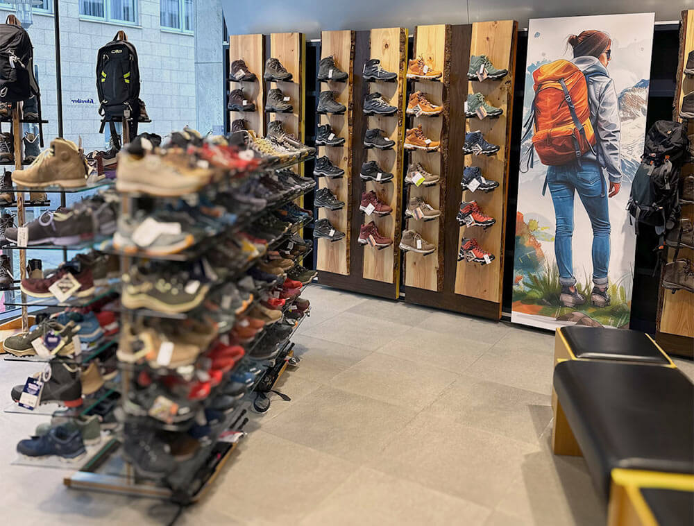 Wanderschuhabteilung bei Schreiber Schuhe Siegen:
große Auswahl an Wander- und Trekkingschuhen auf rustikalen
Holzregalen, mit dekorativem Wander Poster im
Schuhfachgeschäft Siegerland