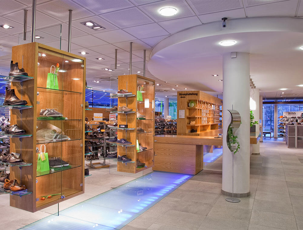 Innenansicht von Schreiber Schuhe in Siegen: moderne
Verkaufsfläche mit beleuchteten Holzregalen, großer
Schuhauswahl und Strumpfabteilung im Schuhfachgeschäft
Siegerland
